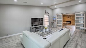 A spacious living room with a white sofa, a glass coffee table, and a fireplace. - Collins Family-Friendly Texas Home with Private Pool! (Garland)