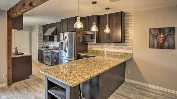 A modern kitchen with dark wood cabinets, granite countertops, stainless steel appliances, and pendant lighting. - Collins Family-Friendly Texas Home with Private Pool! (Garland)