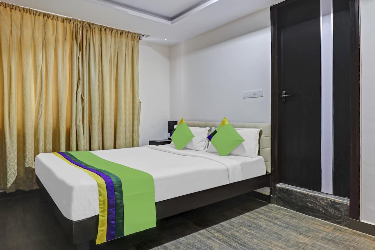 A hotel room with a bed, a nightstand, a lamp, and a door.