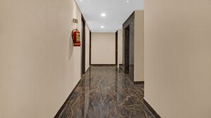 A hallway with a marble floor, a fire extinguisher on the wall, and a door at the end. - Treebo JJ Residency (Bengaluru)