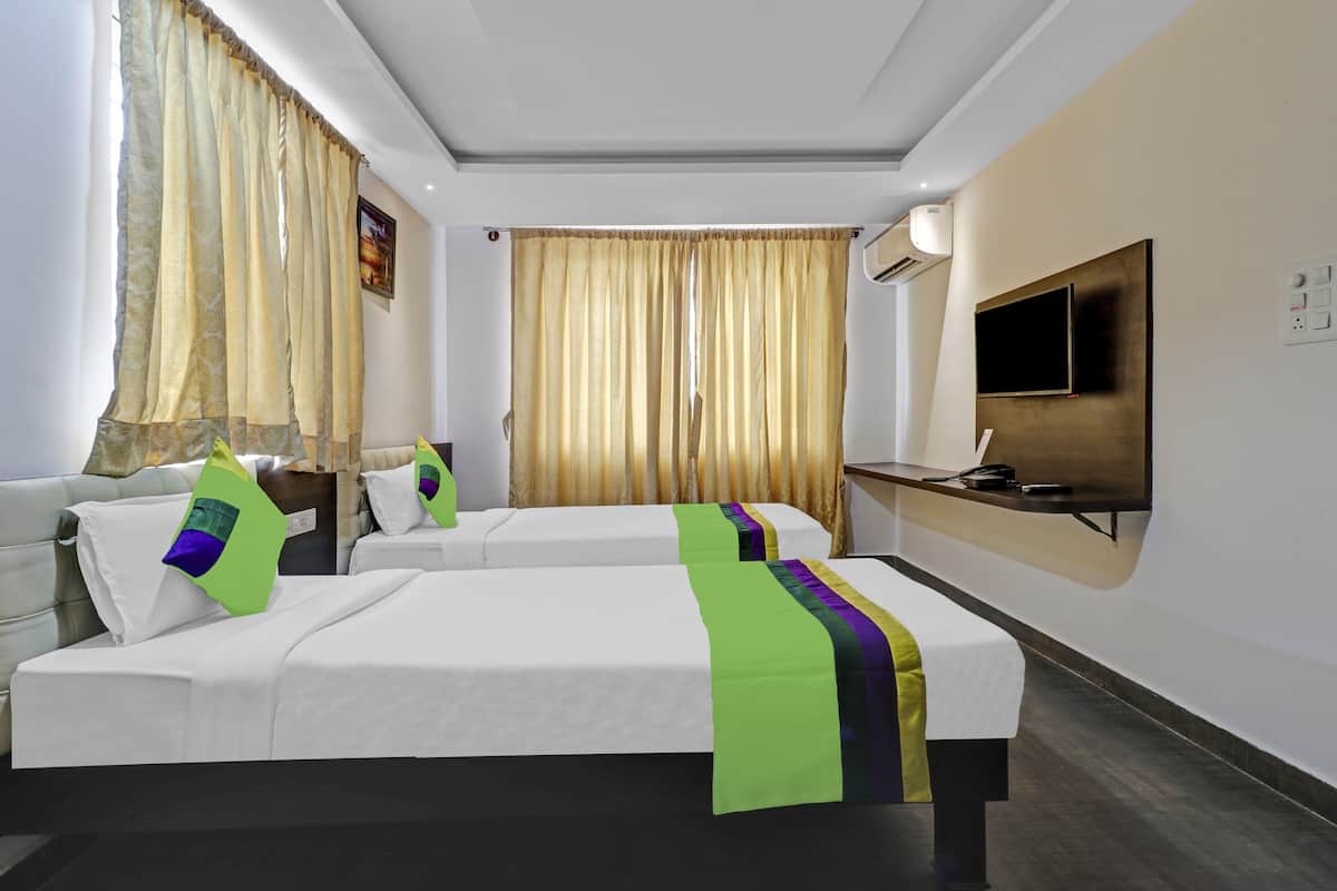 A hotel room with two beds, a TV, an air conditioning unit, and a desk with a phone.