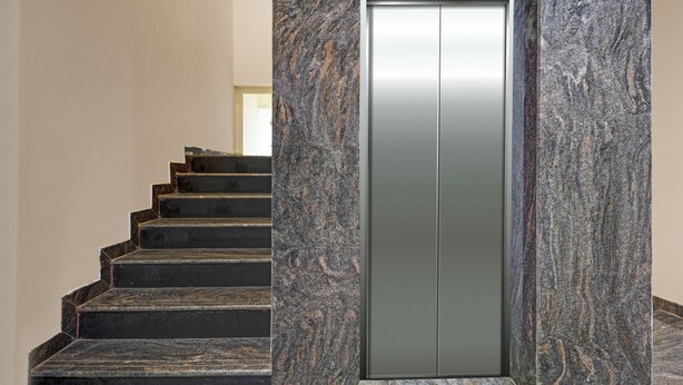 A modern elevator with a metallic finish, surrounded by a granite staircase. - Treebo JJ Residency (Bengaluru)