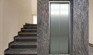A modern elevator with a metallic finish, surrounded by a granite staircase. - Treebo JJ Residency (Bengaluru)