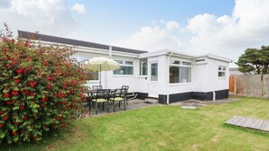 Een wit huis met een tuin, een terras met een tafel en stoelen, en een rood bloeiend struik.