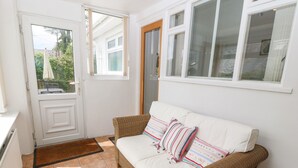 Een gezellige kamer met een witte bank, een deur naar buiten en een raam met gordijnen.