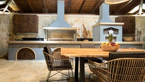 A rustic kitchen with stone walls, a wooden ceiling, and a large central stove.