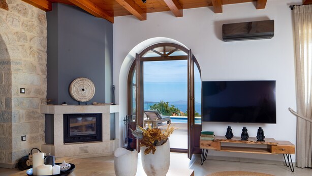 A modern living room with a stone wall, a fireplace, a large TV, and a view of the sea.