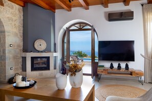 Un salon moderne avec un mur en pierre, une cheminée, un grand téléviseur et une vue sur la mer.