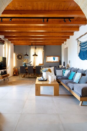 Un salon spacieux avec un plafond en bois, un canapé gris, une table à manger avec des chaises et une table basse.