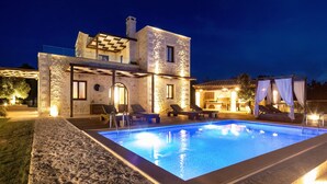 A modern villa with a swimming pool, stone walls, and outdoor seating by the pool.