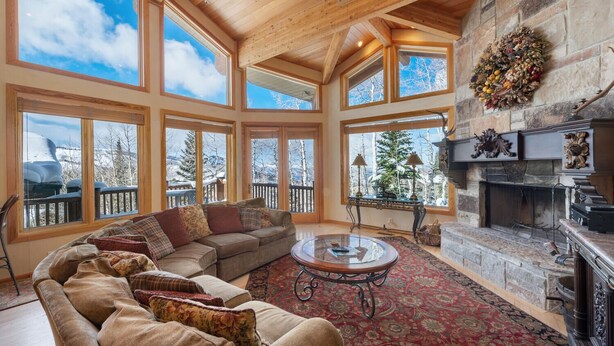 A spacious living room with a large wooden ceiling, a stone fireplace, and multiple large windows offering views of a snowy landscape. - Double Eagle by Park City Vacations (Park City)