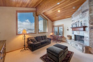 Un salon chaleureux avec une cheminée en pierre, un plafond en bois et de grandes fenêtres.
