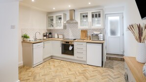 A modern kitchen with white cabinetry, a herringbone wood floor, and built-in appliances. - A Mor (Llanfairpwllgwyngyll)