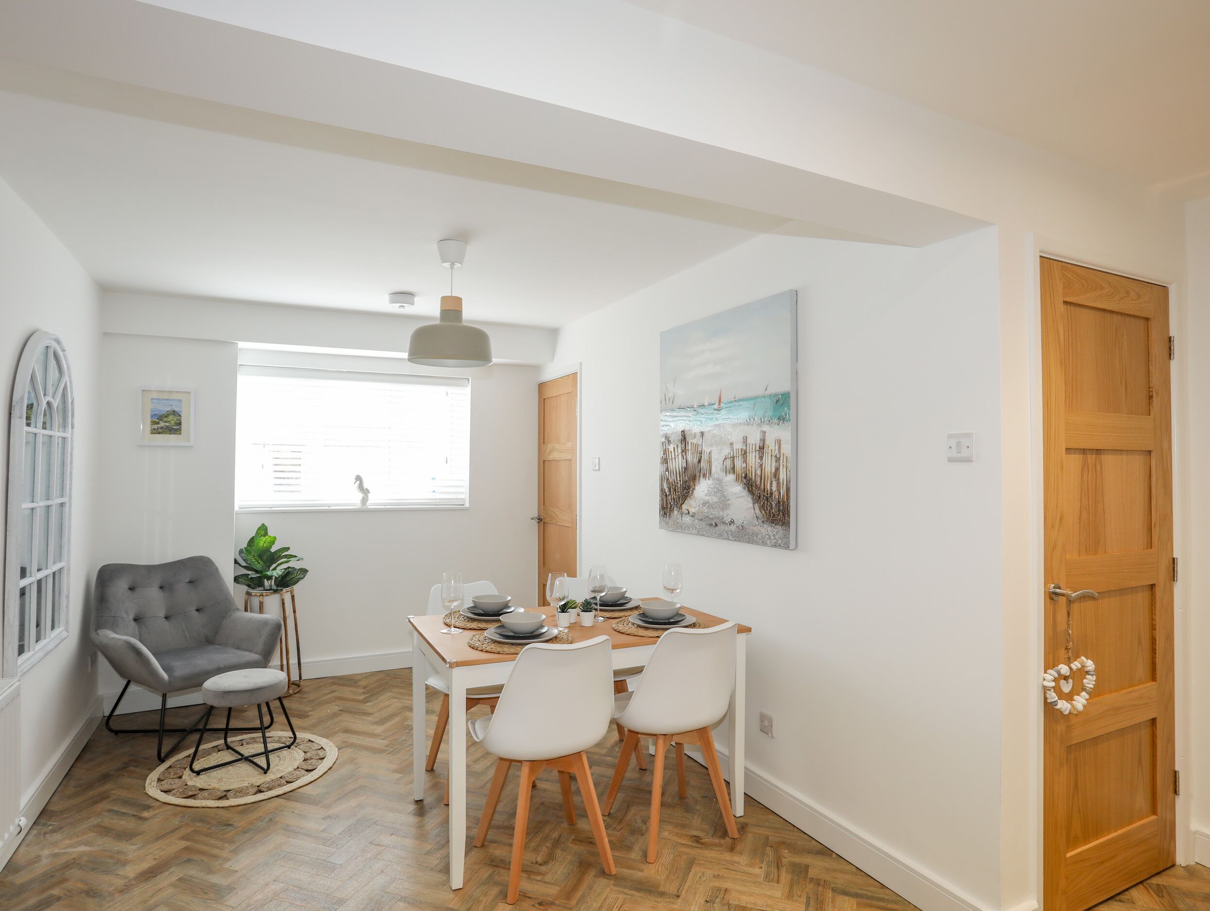 Un comedor con una mesa dispuesta para cuatro, un sillón gris y piso de madera.