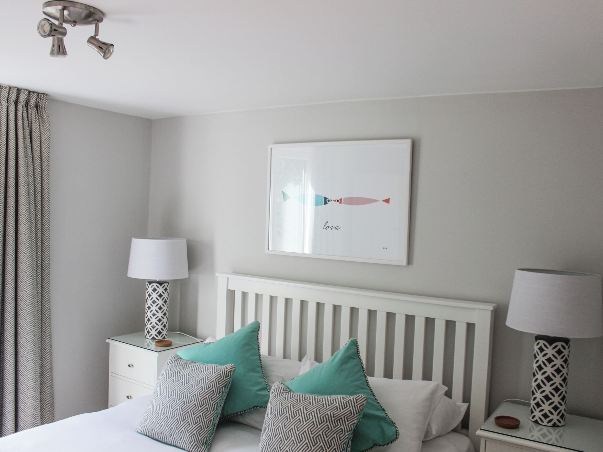 Une chambre à coucher avec un lit, deux tables de chevet avec des lampes, un tableau accroché au mur et une fenêtre avec des rideaux.