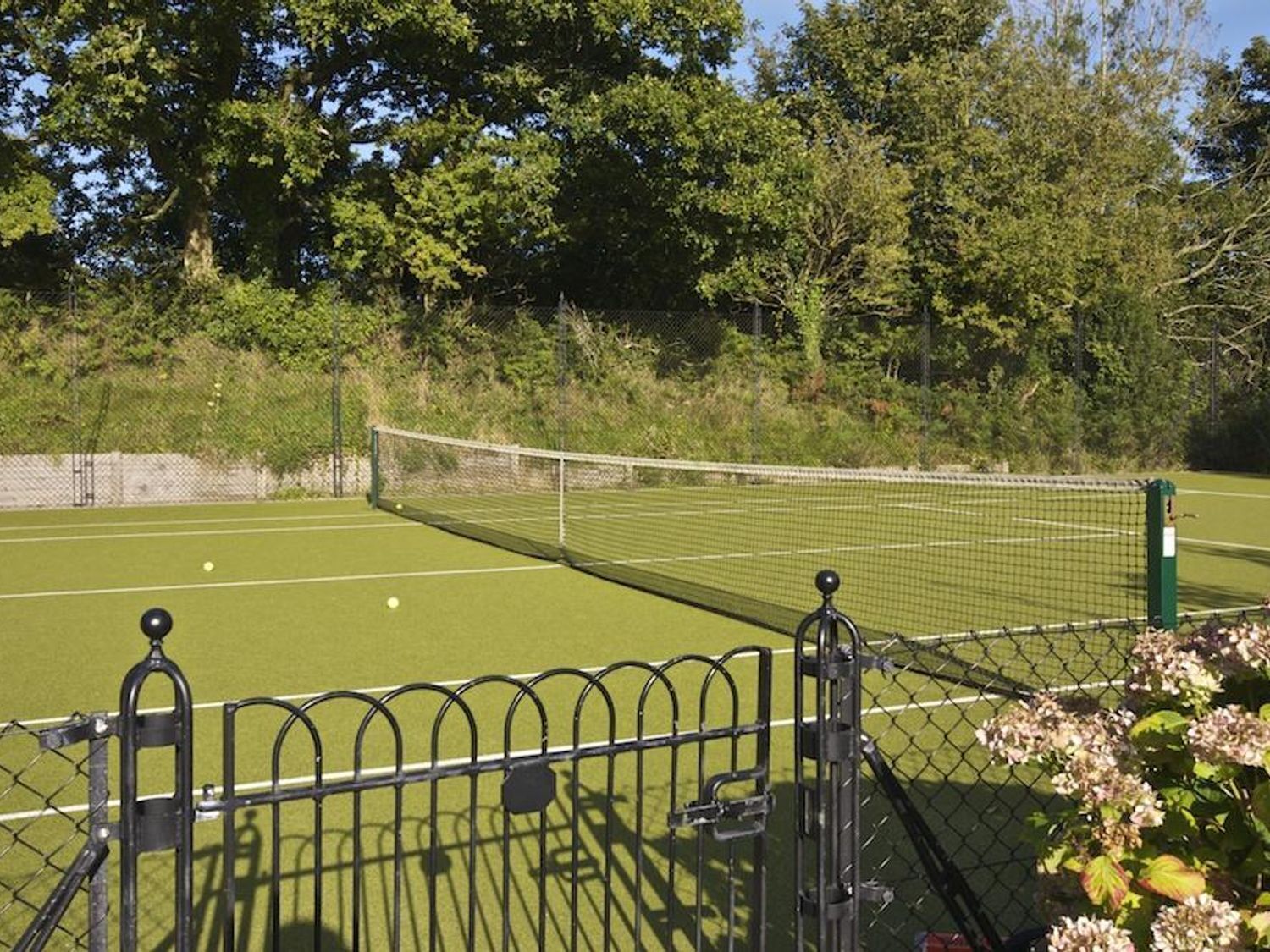 A tennis court with a net, surrounded by a chain-link fence and trees.