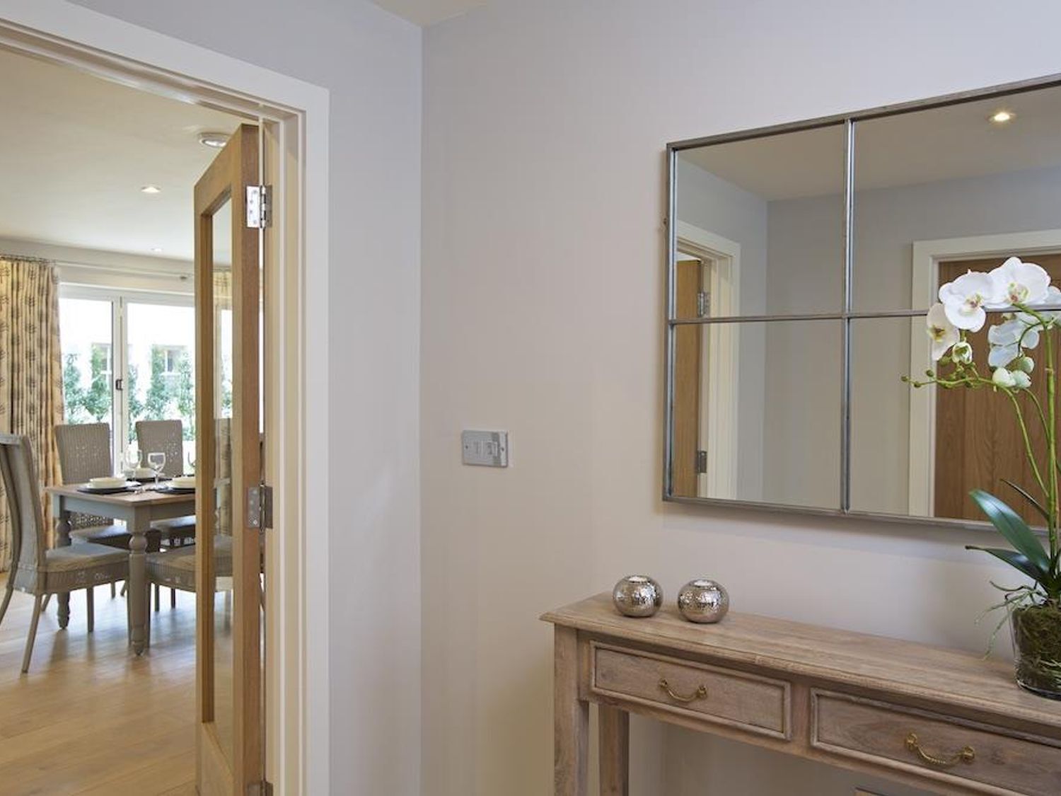 A room with a wooden console table, a large mirror, and a potted orchid.
