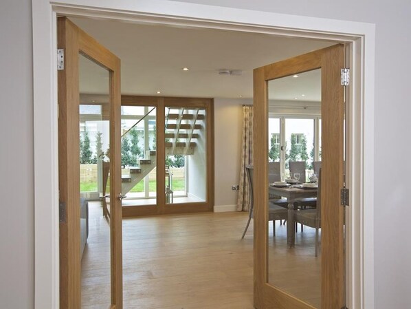 A spacious room with a wooden floor, a dining area with a table and chairs, and a staircase leading to an outdoor area.