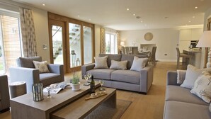 A spacious living room with a grey sofa set, a wooden coffee table, and a dining area in the background. - 3 The Drive, Hillfield Village (Dartmouth)