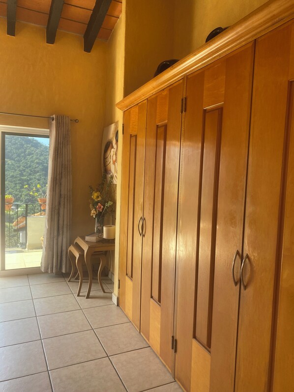 Una habitación con un armario de madera, una mesa con un florero y vistas a un balcón con cortina.