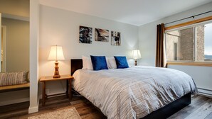 Une chambre à coucher avec un lit, deux tables de chevet avec des lampes, un tapis et des œuvres d’art accrochées au mur.