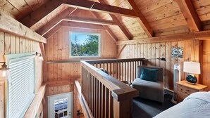 A wooden cabin with a loft bedroom, a balcony, and a view of the forest. - Bear Coast | Cabin w/ Hot Tub, Patio, & Waterview (Ucluelet)