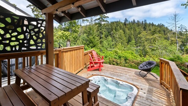 A wooden deck with a hot tub, a red Adirondack chair, and a black lounge chair. - Bear Coast | Cabin w/ Hot Tub, Patio, & Waterview (Ucluelet)