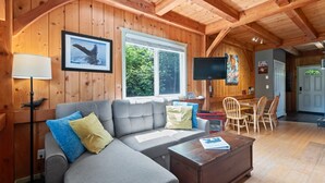 A cozy living room with a sofa, coffee table, and a dining area with chairs and a table. - Bear Coast | Cabin w/ Hot Tub, Patio, & Waterview (Ucluelet)