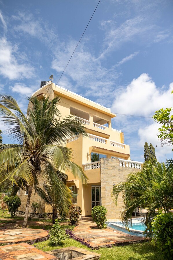 A two-story building with a pool, surrounded by palm trees and a clear sky.