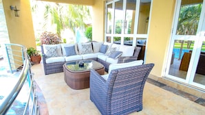 Un patio soleado con un sofá modular, sillones de mimbre y una mesa de centro de cristal.