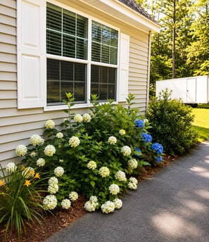 A house with a window, a garden with hydrangea flowers, and a white trailer in the background. - Spacious Home for 14 Guests Near Lake Winnisquam – Close to Everything! (Sanbornton)