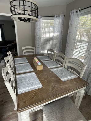 Une salle à manger avec une table en bois, des chaises blanches et un lustre.