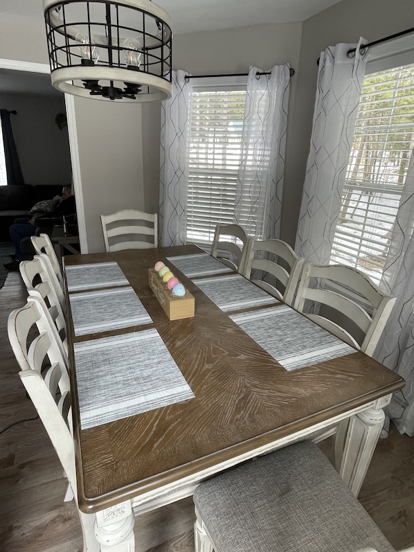 Comedor con una mesa de madera, sillas blancas y una araña.