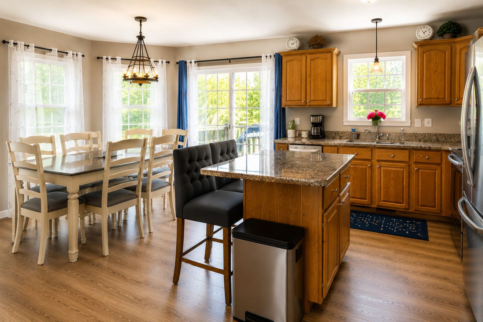 A kitchen with wooden cabinets, a stainless steel refrigerator, a dining table with chairs, and a bar stool.