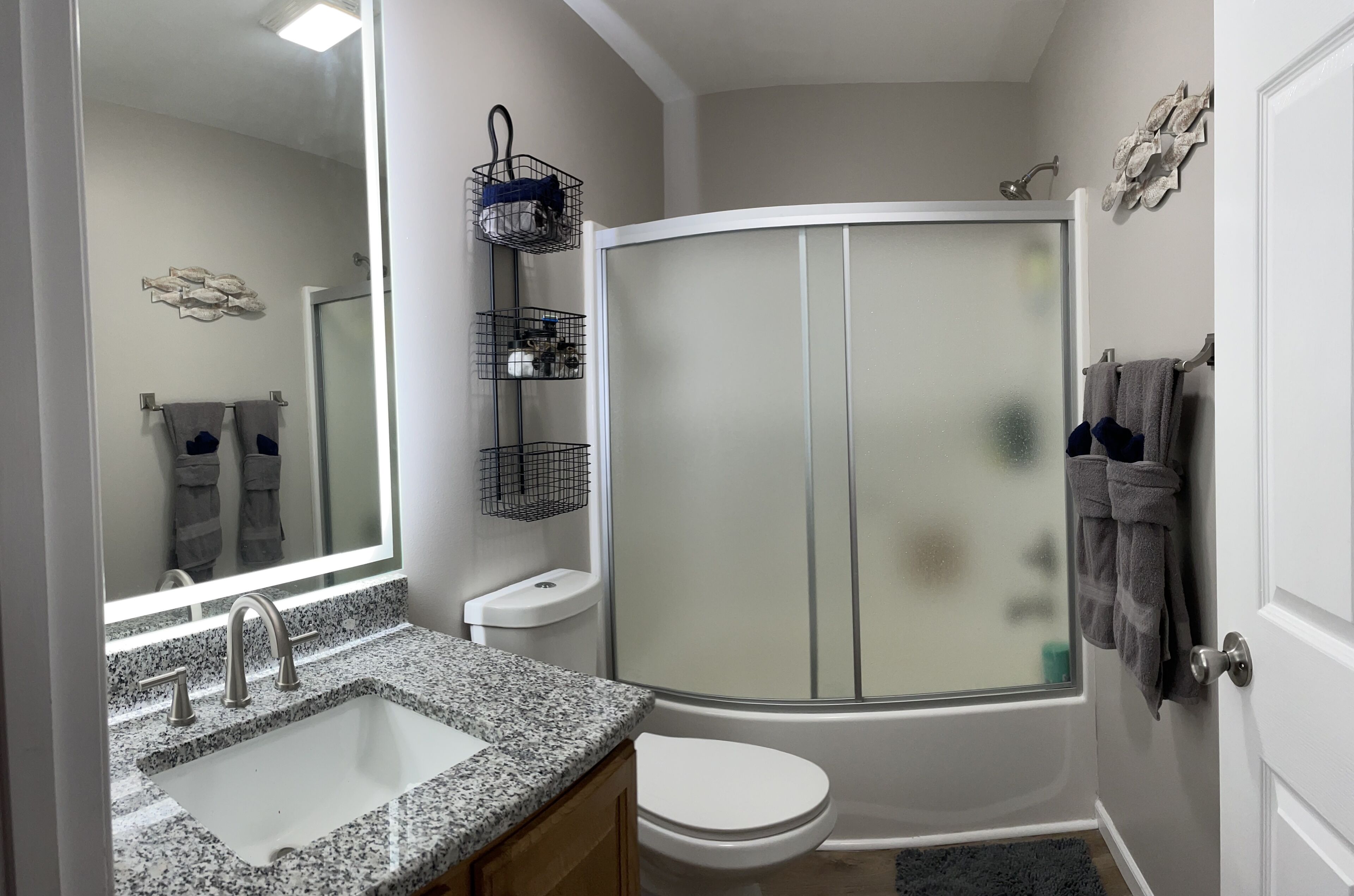 Un baño con lavamanos de encimera de granito, inodoro, ducha con puerta de cristal y espejo sobre el lavamanos.