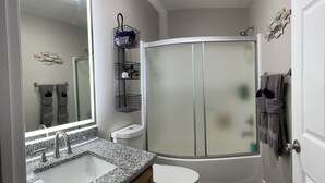 Ein Badezimmer mit Granitwaschtisch, Toilette, Dusche mit Glastür und Spiegel über dem Waschbecken.
