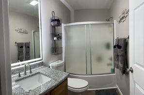 Un baño con lavamanos de encimera de granito, inodoro, ducha con puerta de cristal y espejo sobre el lavamanos.