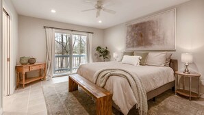 A bedroom with a large bed, a bench, a nightstand, a ceiling fan, and a view through a sliding door. - Glennhouse Getaway (South Haven)