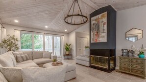 A spacious living room with a large sectional sofa, a fireplace, and a view of the outdoors through large windows. - Glennhouse Getaway (South Haven)