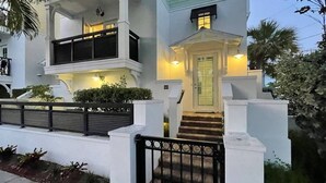 Um edifício de dois andares com fachada branca, uma varanda no andar superior e uma porta de entrada com degraus.