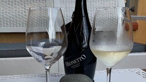 A table with two wine glasses, a bottle of Mionetto prosecco, and a stone on a white table with a metal railing in the background. - 2 Bedroom Apartment in Villasimius (Villasimius)