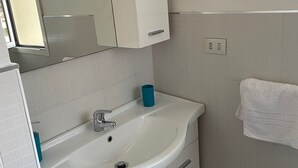 A bathroom with a white sink, a mirror, a towel hanging on the wall, and a blue towel holder. - 2 Bedroom Apartment in Villasimius (Villasimius)