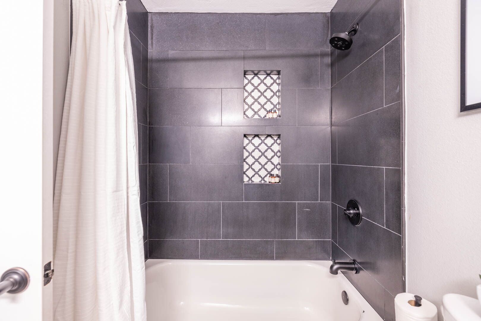 A bathroom with a bathtub, dark tiled walls, and two small windows with decorative patterns.