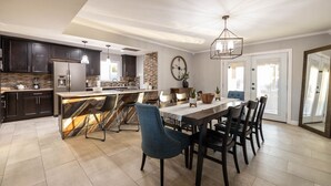 Een ruime keuken met donkere kasten, een marmeren eiland en een eethoek met een grote tafel en stoelen.