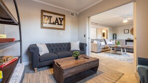 Een woonkamer met een donkergrijze bank, een houten salontafel en een bord met de tekst 'PLAY' aan de muur.