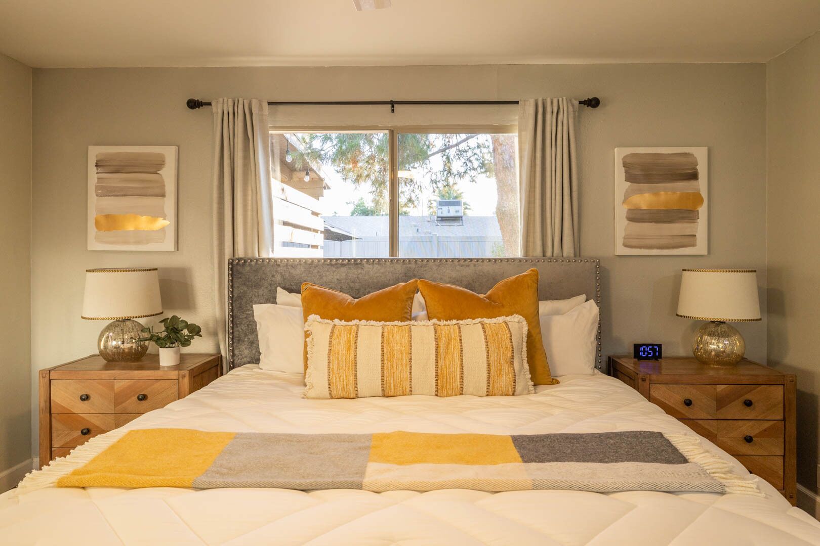 A bedroom with a large bed, two bedside tables, a nightstand, a window with curtains, and wall art.