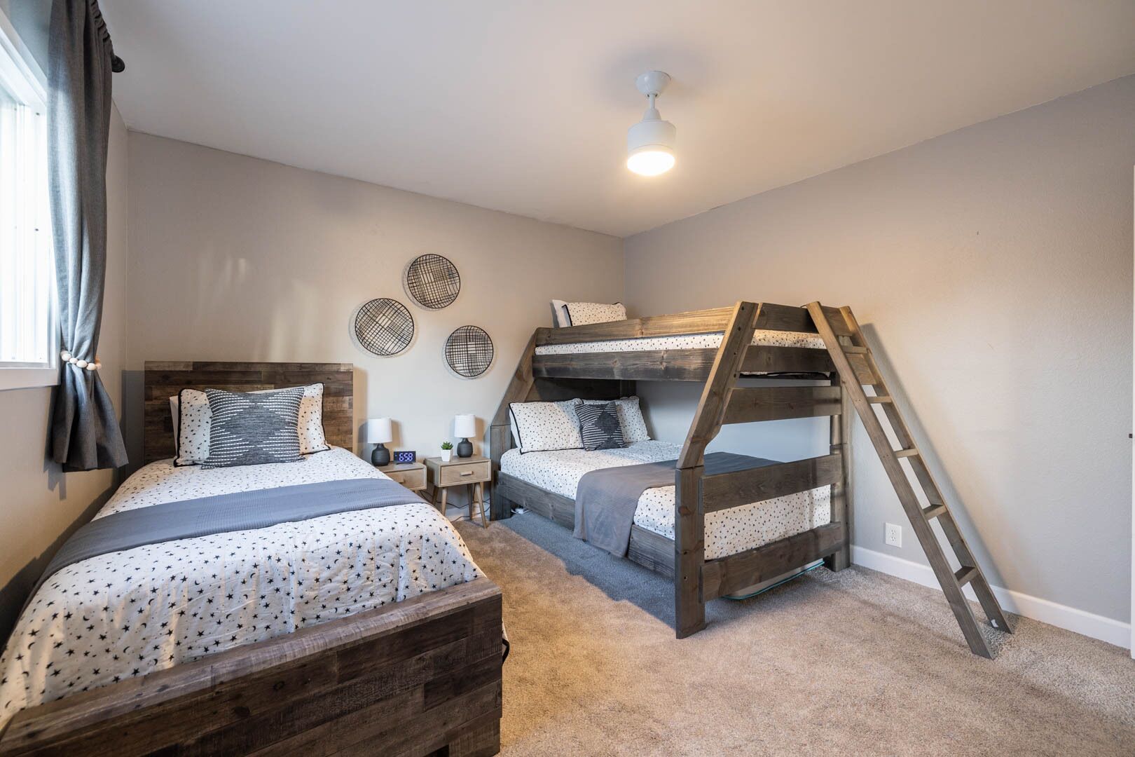 A bedroom with two bunk beds, a wooden ladder, a nightstand with a clock, and a ceiling fan.