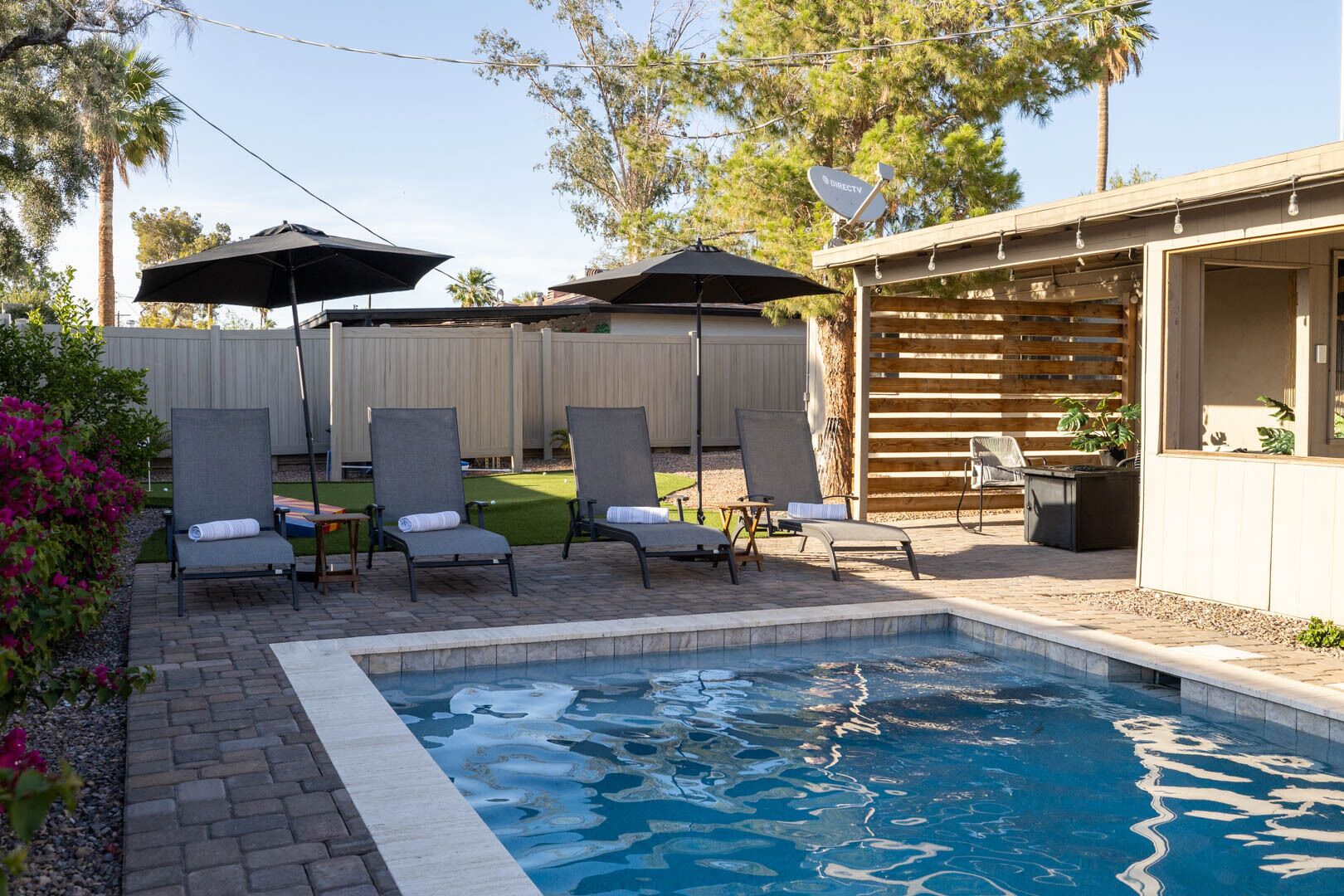 Ein Garten mit Schwimmbad, Liegestühlen und Sonnenschirmen.