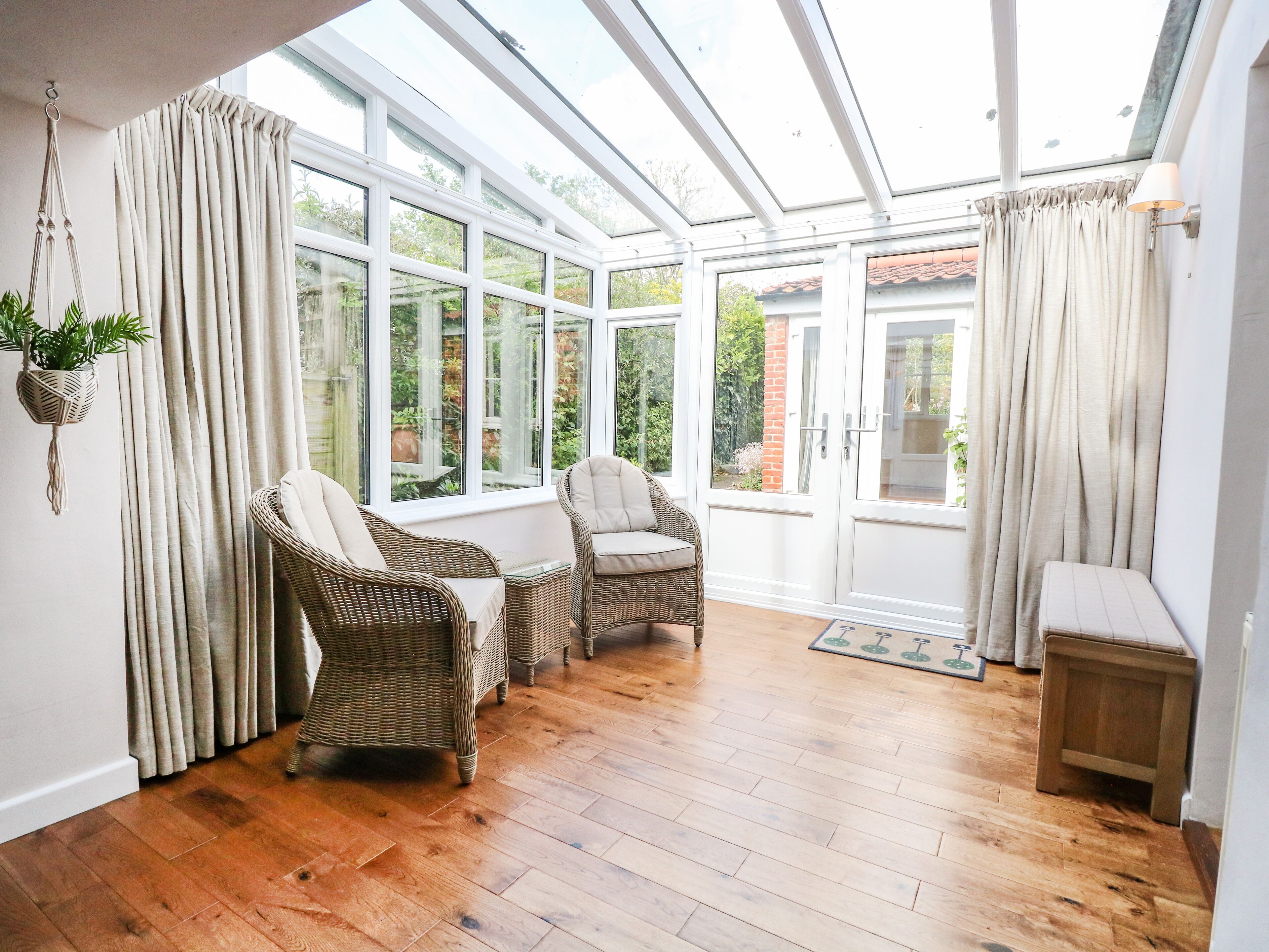 A sunroom with wicker furniture, large windows, and a wooden floor.