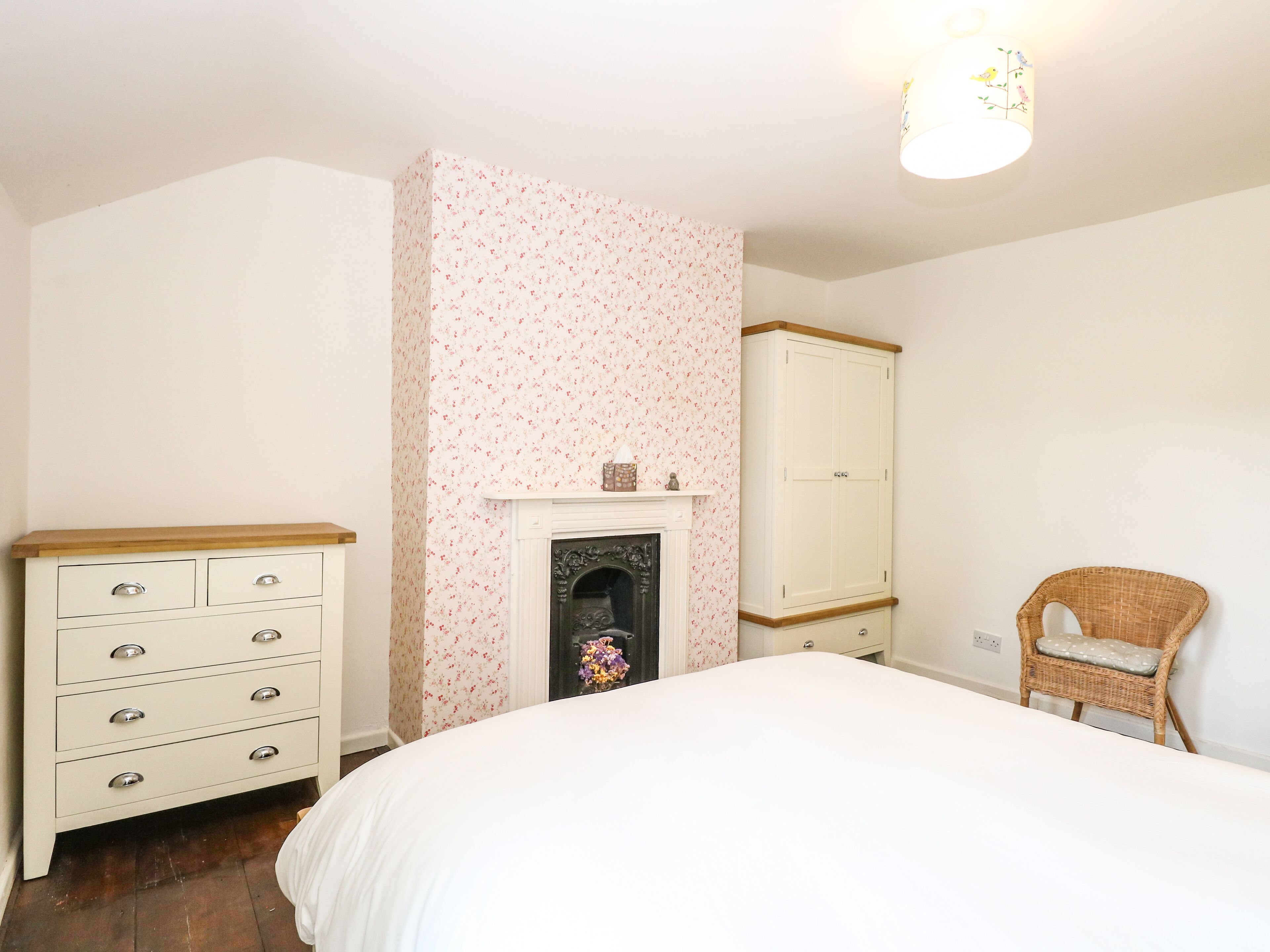 A bedroom with a bed, dresser, wardrobe, and a fireplace.